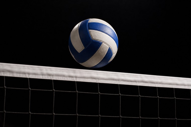 Pallone da pallavolo sospeso sopra la banda bianca della rete in un palazzetto buio